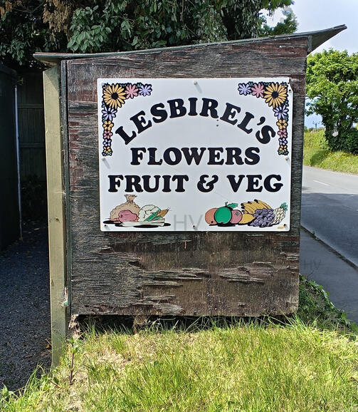 Honesty Farm Shop lesbirel's signage on hte side of an old wooden hedge veg stall. wooden shed surrounded by roses
