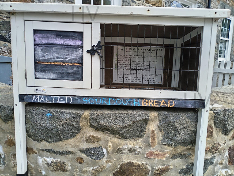 front view of a sour dough bread honesty stall wooden shed surrounded by roses